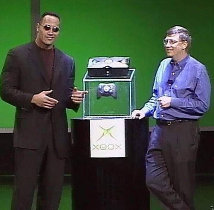 This meme is a screenshot of two people, Dwayne "The Rock" Johnson and Bill Gates, sitting at a table with a console and a game controller. The text "Xbox is a new gaming platform from Microsoft" appears at the bottom of the image, but it's actually a joke setup for a humorous statement. The meme is likely referencing a humorous or ironic situation where someone says "Xbox is a new gaming platform from Microsoft" in a serious tone.